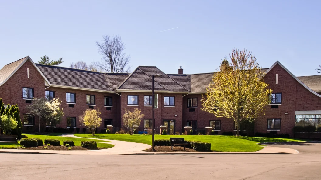 Exterior of modern luxury care home with trees surrounding the building and a green lawn in the foreground.