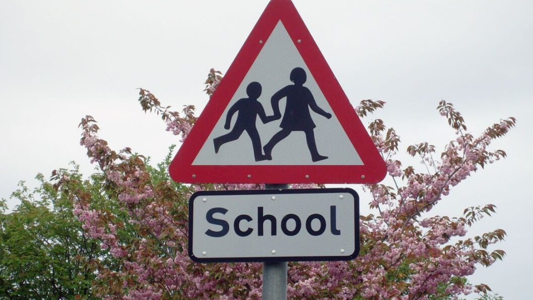 School sign in England with a tree with pink flowers in the background.