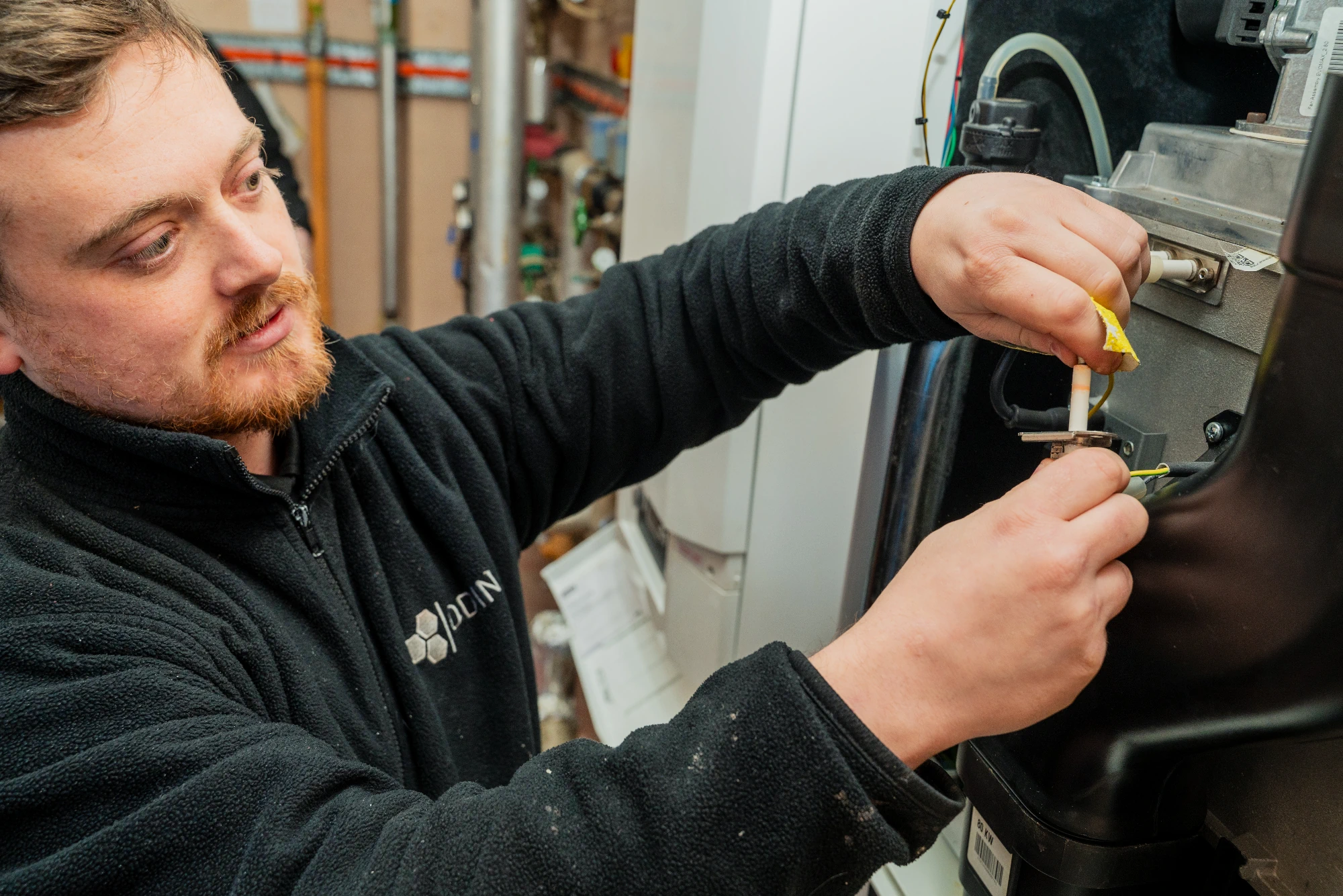 A close-up of an engineer wearing a black ODIN fleece fixing a commercial boiler. 