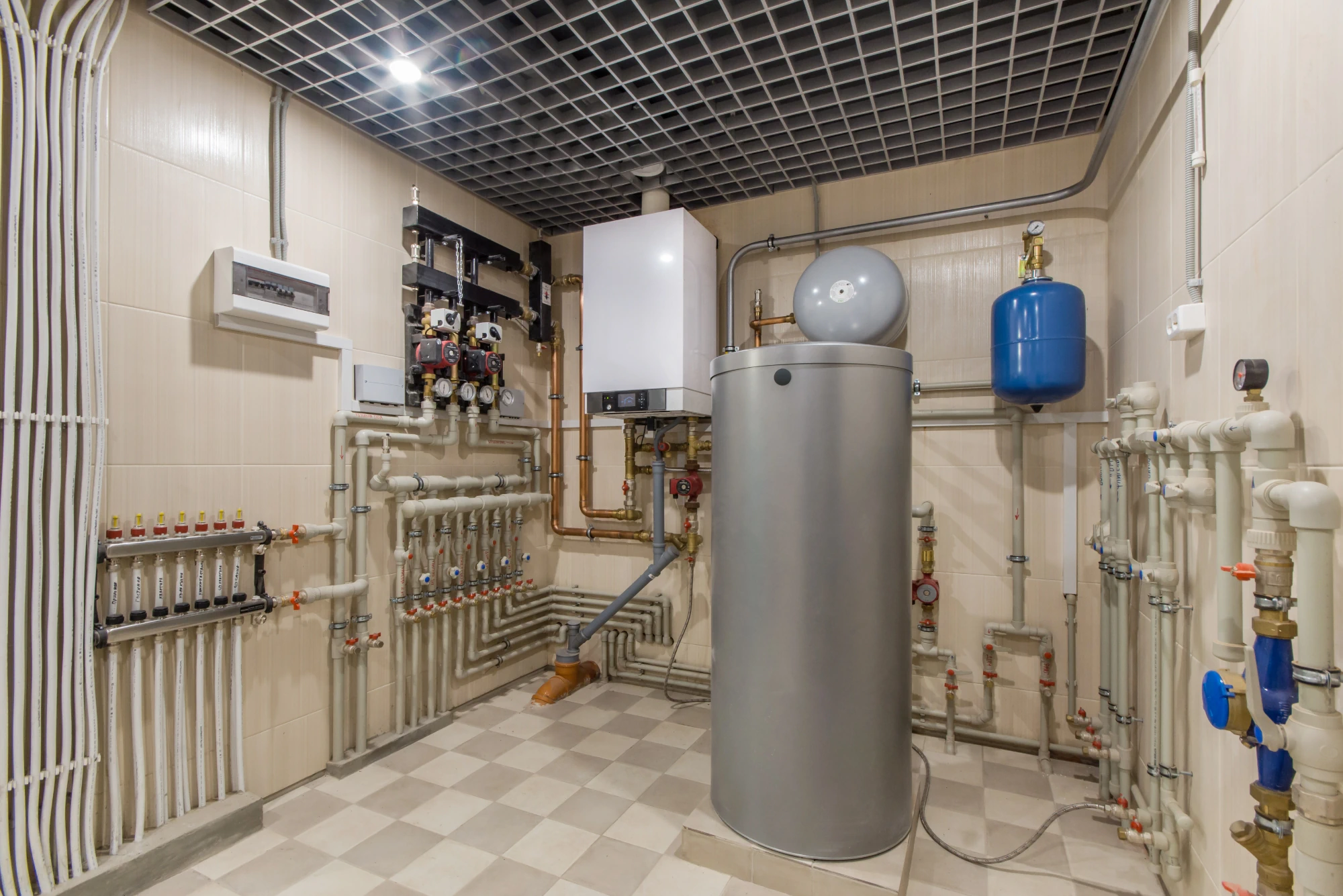 Silver hot water storage cylinder in a large commercial boiler room.